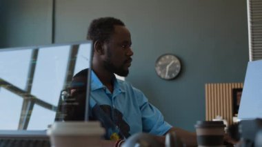 Gündelik tişört giyen genç Afrikalı Amerikalı programcı modern bilişim şirketinin ofisinde bilgisayar üzerinde çalışıyor.