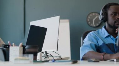 Modern ofiste dizüstü bilgisayar ve masaüstü bilgisayar üzerinde çalışan etnik çeşitlilikte iki genç bilişim uzmanı