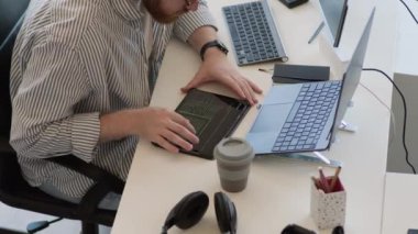 Ofiste kodlama yaparken dijital tablet, laptop ve masaüstü bilgisayarı kullanan meşgul genç Kafkas programcısının yüksek açılı görüntüsü