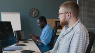 Önde gelen bilişim şirketinin modern ofisinde çalışan beyaz ve siyahi gençlerin yan görüntüsü