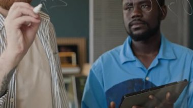 Dijital tablet ekranına bakan ve ofisteki cam duvara kod yazan genç etnik çeşitlilikteki programcılar