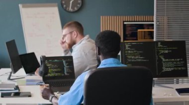 Tanımlanamayan siyah programcının kahve içmesi ve modern ofiste kod üzerinde çalışması arka planda bilgisayar kullanan Kafkasyalı meslektaşı