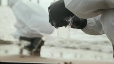 Koruyucu giysili, tanınmayan bir biyokimyacının, endüstriyel rıhtımda toprak örnekleri toplayıp iş arkadaşıyla birlikte araştırma yaparken çantaya koyduğu yakın çekim.