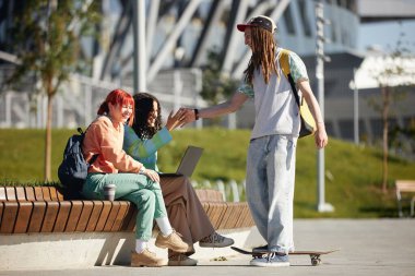 Okuldan sonra parka takılan parlak elbiseli iki gülen kız öğrencinin manzarası. Rastlantılı genç bir erkek kıza beşlik çakıyor. Öğrenciler kampüste şakalaşıyor.