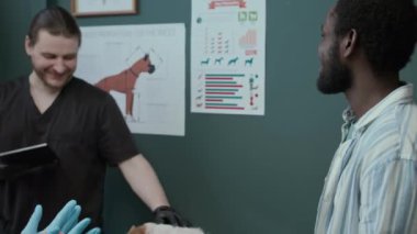 Beyaz kadın veteriner önlük ve eldiven giyer idrar kesesi düzenini kullanır ve Afrikalı Amerikalı erkek köpek sahibine klinikte randevu verir.