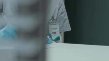 Modern ofisteki beyaz masada otururken önlüklü ve azot eldivenli tanınmayan kadın veterinerin tıbbi belgelere yazdığı sahneler.