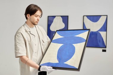 Modern sanat galerisi fotokopi alanında sergi açmayı planlarken genç bir adamın minimum bel üstü portresi özenle soyut sanat eserlerini tutuyor.