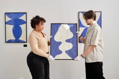 Modern sanat galerisinde sergiye hazırlanırken soyut mavi şekilli iki kişinin yan görünüşü