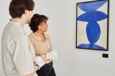 Sergiye hazırlanırken ve beyaz eldiven giyerken soyut sanat eserlerine bakan iki sanat galerisi işçisinin yan görünüm portresi