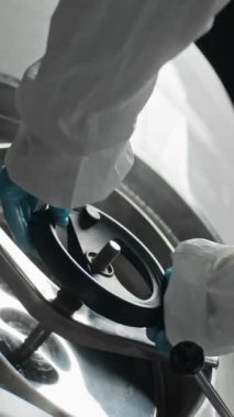 Bira fabrikasındaki büyük metal tankın üzerinde mavi nitril eldiven ve koruyucu giysi giymiş, tanınmayan işçilerin düşük açılı dikey çekimleri.