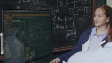 Siyah ekranda karmaşık arayüzle ekranı gösteren Kafkasyalı genç kızın orta boy fotoğrafı ve ders sırasında programlama öğretmeniyle yazılım geliştirme tartışması.