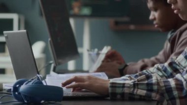 Bilgisayarın ve dizüstü bilgisayarın önünde oturmuş modern sınıflarda kodlama ve programlama okuyan iki çok ırklı gencin göğüs kafesi.