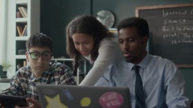 Genç siyahi erkek öğretmen ve çeşitli gen z öğrencilerinin ders sırasında dizüstü bilgisayarda kodlama ve programlama çalışmaları.