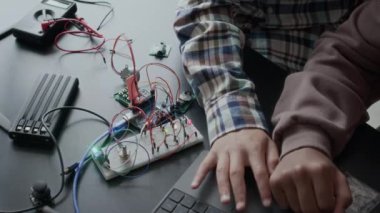 Yukarıda, sınıftaki elektronik projesini hazırlarken dizüstü bilgisayar kullanan ve devre kartı ayrıntıları ve kablolarıyla çalışan tanınamayan iki genç öğrencinin yukarıdaki çekimlerinden.