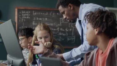 Modern sınıfta teknoloji veya robotik projesinde yer alan çok ırklı genç öğrencilere yardım eden Afrikalı Amerikalı erkek öğretmen