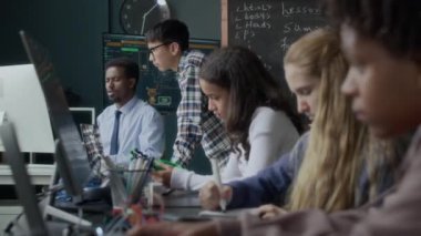 Modern sınıfta genç siyahi erkek öğretmenlerden robotik ve kodlama dersi alan etnik çeşitliliğe sahip gençler.