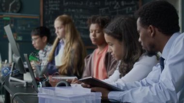 Modern sınıfta siyahi erkek öğretmenlerin rehberliğinde teknoloji ve mühendislik projelerinde işbirliği yapan çoklu etnik gruptan öğrencilerin göğüs göğüse çekimleri.
