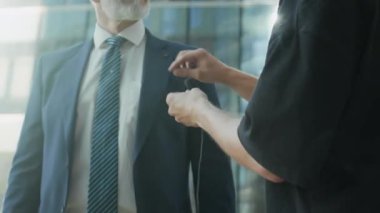 Şehir merkezindeki cam binaya karşı açık havada kayıt yapmaya hazırlanırken küçük mikrofonu haber sunucusunun yakasına takan tanınmayan ses teknisyeninin görüntüsü.