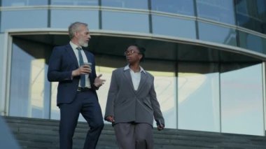 Modern ofis binasının merdivenlerinden inerken çok ırklı ve şık bir iş kadını ile sohbet ediyorlar.