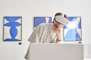 Müzedeki modern sanat sergisi sırasında görünmez dijital sanat eserlerine bakarken VR kullanan düşünceli bir adamın minimum portresi.