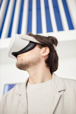 Minimum modern sanat müzesi ortamında VR kulaklık takan bir adamın dikey yan görünümü