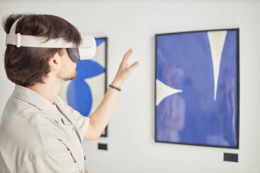 Modern sanat fuarında VR giyen bir adamın resimlerle etkileşimli karışık gerçekliğin tadını çıkarması, kopyalama alanı