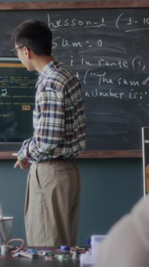 Genç Asyalı öğrencilerin ekran ekranında pinpon oynarken ve öğretmenle modern sınıfta ders alırken yazılım mühendisliği tartışırken dikey orta pozu.