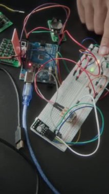 Sınıfta birlikte elektronik projesinde çalışırken devre kartına kablo bağlayan tanınmayan öğrencilerin dikey yakın çekimi.