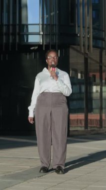 Şehir merkezindeki güneşli caddede dikey olarak duran siyahi kadın TV haberlerini sunuyor.