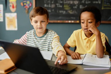 Farklı etnik kökenlere sahip iki çocuk dizüstü bilgisayarda tarama bilgilerine bakıyor. Sınıfta teknoloji kullanımına tamamen bağlı, kopyalama alanı.