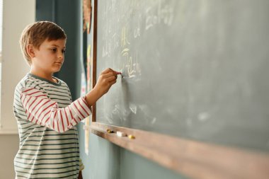 Okuldaki karatahtaya özenle mektup yazan konsantre genç bir çocuğun yan görüntüsü, gelişigüzel öğrenme sahnesi, kopyalama alanı