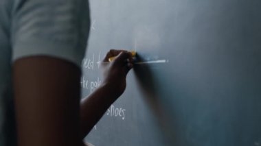 Sınıfta İngilizce dersinde boşluğu doldururken kara tahtaya yazı yazan tanınmamış Afrikalı Amerikalı erkek öğrencinin görüntüsü.