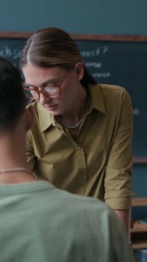 Kafkas kadın İngilizce öğretmeninin tahtada oturan ve dinleyen çok ırklı üniversite öğrencilerine konuyu açıklarken orta boy dikey görüntüsü.