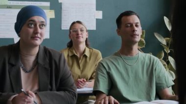 Modern sınıfta masa başında oturan ve ders sırasında öğretmenle etkileşimli tartışmalar yapan genç yetişkin erkek ve bayan öğrencilerden oluşan etnik çeşitliliğe sahip bir grup.