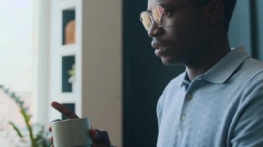 Genç siyahi erkek İngilizce öğretmeninin elinde yapışkan not ve fincanla sınıftaki bir grup öğrenciye kelime haznesini nasıl hızlı öğreneceğini açıklarken çekilmiş bir fotoğrafı.