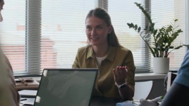 Genç beyaz kadın İngilizce öğretmeni, çok ırklı bir grup öğrenciye interaktif bir ders veriyor, modern sınıfta birlikte oturuyor ve tartışıyorlar.