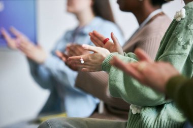 Önplanda görülen etkileşimli atölye çalışması sırasında el çırpan bir grup insan, arka planda çeşitli kişilerle el ele tutuşmaya odaklanıyor