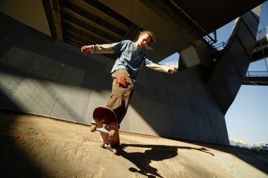 Bir üst geçidin altında ustalıkla kaykay yapan genç insan, arka plandaki endüstriyel yapılarla etkileyici bir denge göstererek dinamik şehir sahnesini yakalıyor.