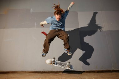 Kaykaycının havada donma anı, kaykay üzerinde etkileyici bir numara sergiliyor. Duvarda gölgeler var. Dinamik ve dramatik bir sahne oluşturuyor.