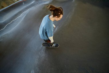 Kapalı alandaki kaykay parkında kavisli rampaları ve düz asfalt yüzeyi olan uzun saçlı biri.