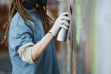 Koruyucu maske takan sanatçı, şehir duvarında sprey boyayla canlı bir sokak sanatı yaratıyor. Günlük giysiler içinde sanatçı, kesintisiz bir şekilde etkileyici graffiti yapmaya odaklanıyor.