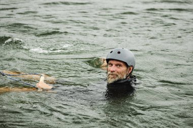 Gölde sörf yaparken suya düşen sakallı adamın portresi ve fotokopi makinesine gülümsüyor.