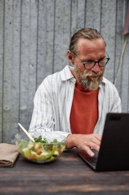 Laptop kullanan ve arka planda çalışırken veya internet metal duvarı kullanırken gözlük takan modern beyefendinin dikey portresi.