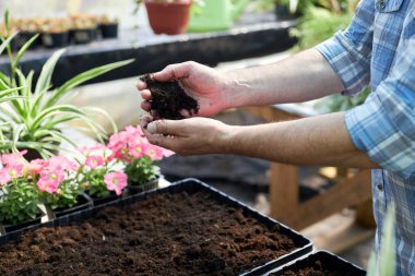 Bahçeye çiçek ekmeye hazırlanırken elleri toprağı tutan insanlar bahçecilik tekniği ve tutkusunu gösteriyor.