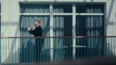 Kafkasyalı genç iş adamı cep telefonuyla konuşuyor modern iş merkezinin koridorunda cam korkuluklarda yürürken sonra da tuhaf bir şekilde dans etmeye başlıyor.