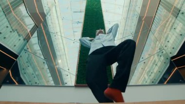 Kırmızı çoraplı ve ofis kıyafetli bir erkek dansçının modern kapalı alanda cam duvarlar ve tavanlı solo performans sergilediği alçak açılı fotoğraf.
