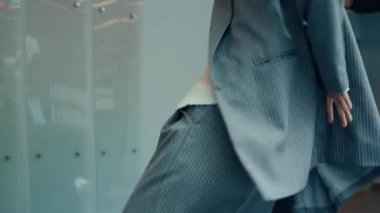 Çizgili gri takım elbiseli, kendine güvenen beyaz bir iş kadını koridor boyunca bavul taşıyor ve tuhaf hareketlerle tuhaf danslara başlıyor.