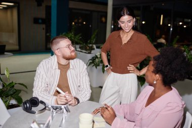 Kafe masasında oturan iki iş arkadaşından oluşan çeşitli yaratıcı ekip destekleyici bayan patronla birlikte ofis merkezindeki çalışma sürecini kontrol ediyor, kamera flaşı.