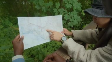 İki çok ırklı sırt çantalı erkek arkadaş, yeşil ormanda yaz yürüyüşü sırasında haritada rotayı tartışıyorlar.