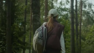 Sırt çantalı kadın turistin gündüz vakti ormanda yürüdüğü arka plan görüntüsü.